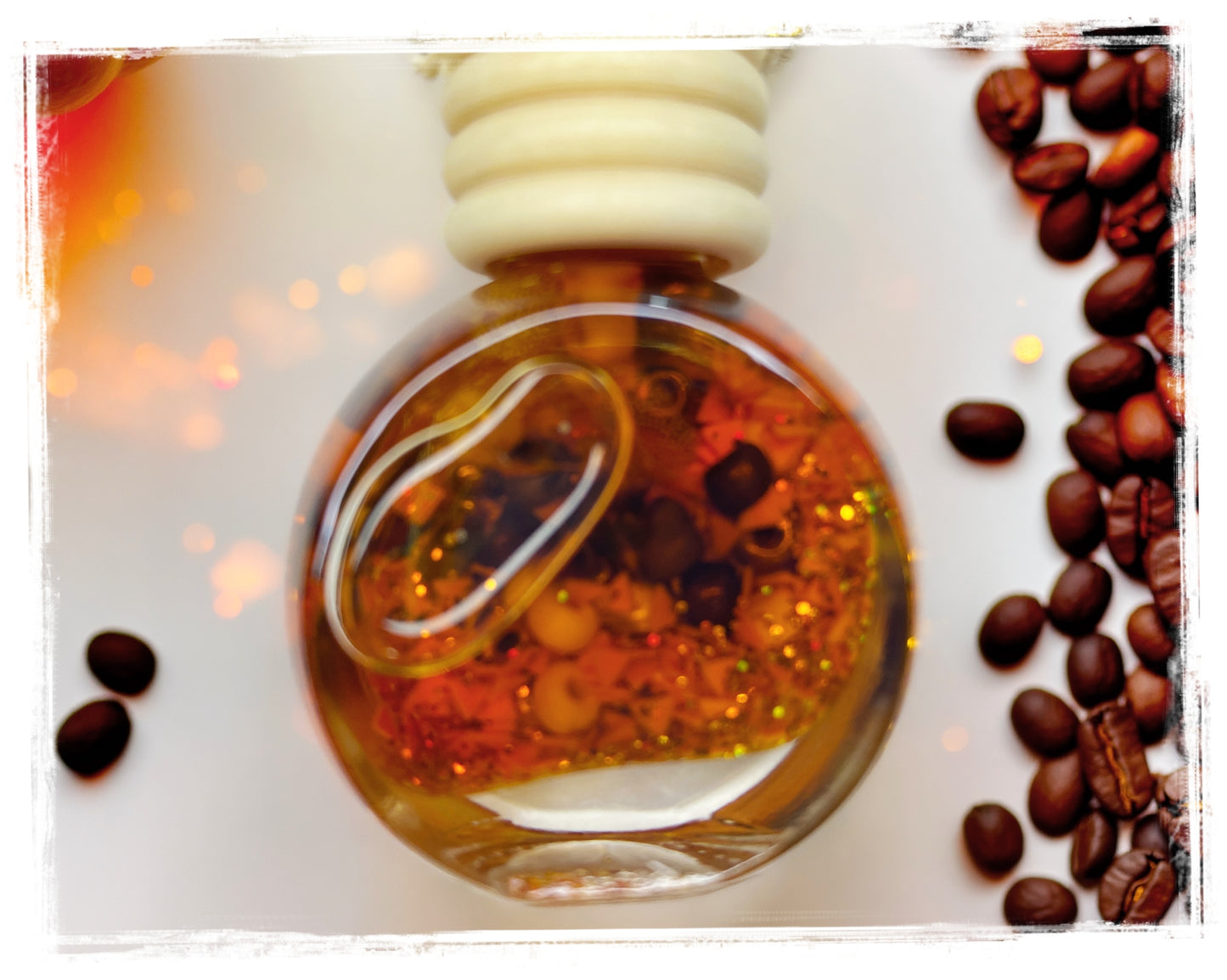 Pumpkin Spice Latte car charm – round glass bottle with deep amber oil, red botanicals, and gold glitter surrounded by coffee beans