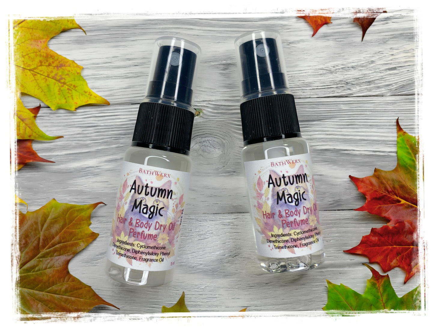 BathWerx Autumn Magic Hair & Body Dry Oil Perfume - two mini spray bottles with floral autumn label on a rustic white wood background surrounded by fall maple leaves