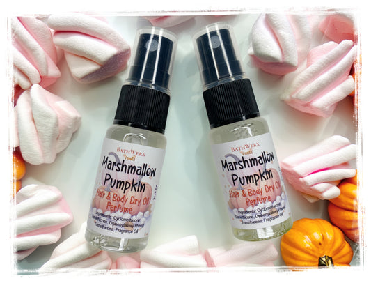 Two BathWerx Vanilla Marshmallow Pumpkin Hair & Body Dry Oil Perfume spray bottles on a white surface, surrounded by pink and white twisted marshmallows and mini orange pumpkins