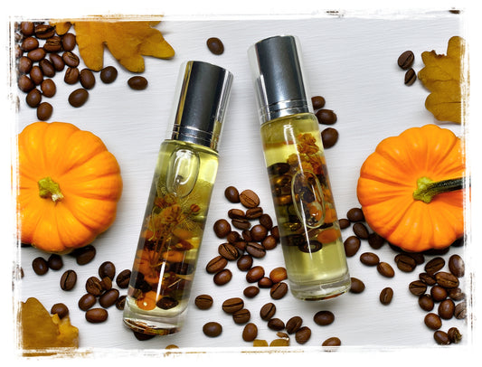 Two BathWerx Pumpkin Spice Latte Roll-on Perfume Oil bottles with silver caps, filled with golden oil, coffee beans, and orange botanicals, styled on a white surface with mini orange pumpkins, scattered coffee beans, and golden fall leaves