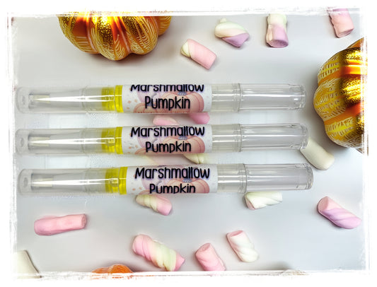 Three Marshmallow Pumpkin Moisturizing Nail Pens displayed horizontally on a white surface, surrounded by pink and white marshmallows and gold decorative pumpkins