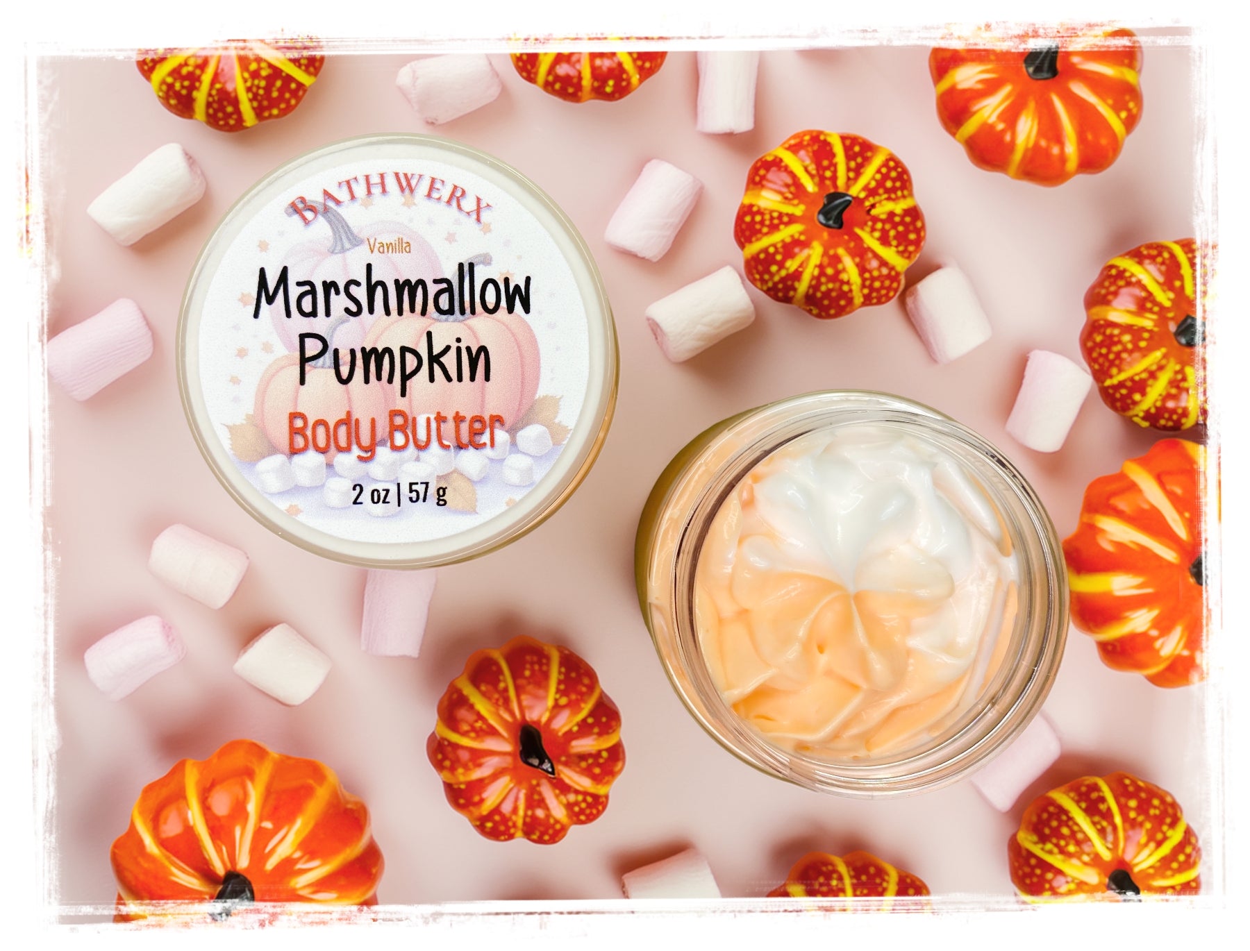 BathWerx Vanilla Marshmallow Pumpkin Body Butter 2 oz jar with swirled orange and white whipped texture, surrounded by mini pumpkins and pastel marshmallows on a blush pink background.