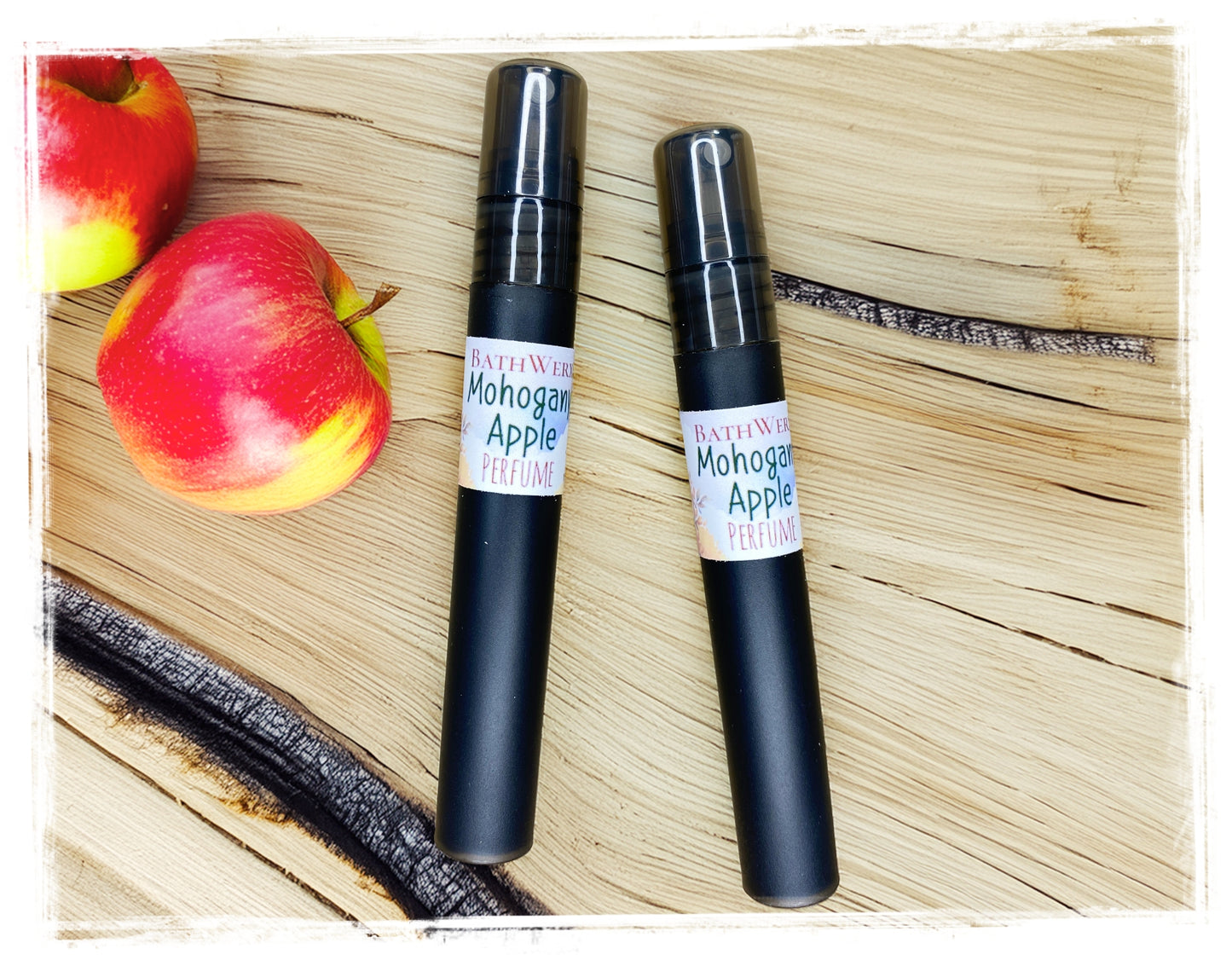 BathWerx Mahogany Apple perfume sprays in matte black, styled on a rustic wood surface with fresh red and yellow apples - travel-size 10ml fall fragrance