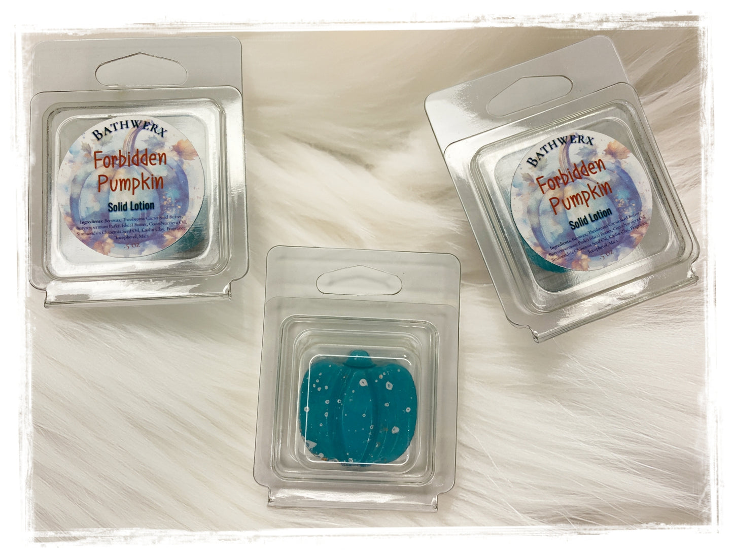 Two BathWerx Forbidden Pumpkin Solid Lotion clamshell packages alongside an unwrapped teal lotion bar with white speckles, displayed on a soft white faux fur surface.