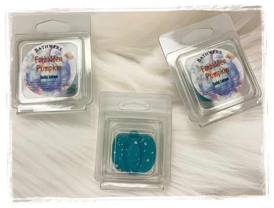 Two BathWerx Forbidden Pumpkin Solid Lotion clamshell packages alongside an unwrapped teal lotion bar with white speckles, displayed on a soft white faux fur surface.
