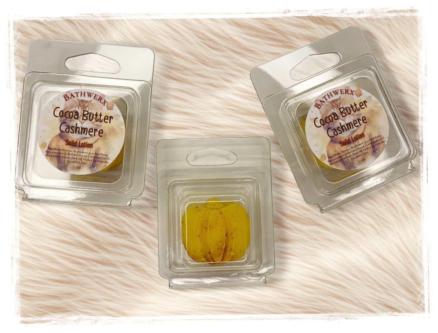 Two BathWerx Cocoa Butter Cashmere Solid Lotion Bar clamshell packages alongside an unwrapped golden lotion bar, displayed on a soft white faux fur surface.