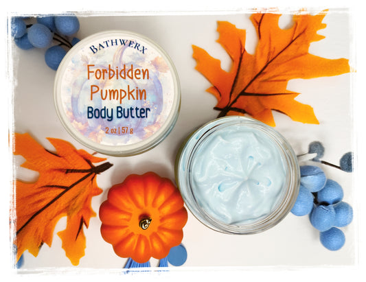 Flat lay of BathWerx Forbidden Pumpkin Body Butter 2 oz jar — lid labeled and open jar showing light blue whipped cream texture, styled with orange autumn leaves, a mini pumpkin, and blue berry accents