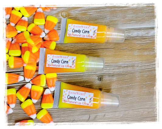 BathWerx Candy Corn All-Natural Lip Gloss tubes on a rustic wood background surrounded by candy corn.