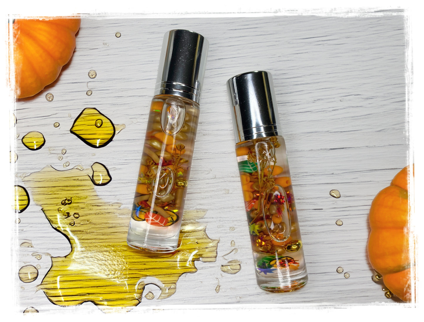 Two BathWerx Pumpkin Lager roll-on perfume oil bottles filled with amber oil and colorful botanicals, displayed on a white wood surface surrounded by orange pumpkins and golden oil droplets.