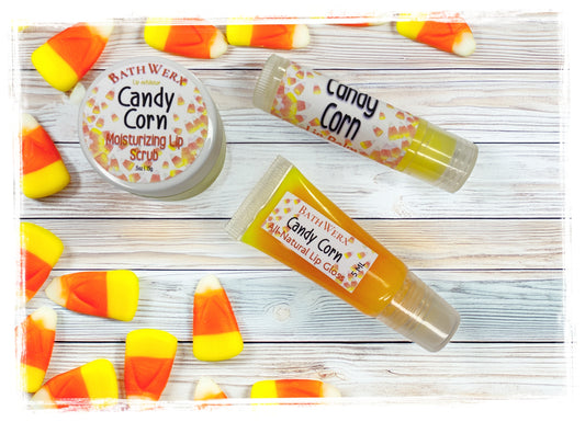 BathWerx Fall Candy Corn Lip Kit displayed on a white wood surface surrounded by candy corn, featuring a Candy Corn Moisturizing Lip Scrub tin, Candy Corn Lip Balm stick, and Candy Corn All-Natural Lip Gloss tube.