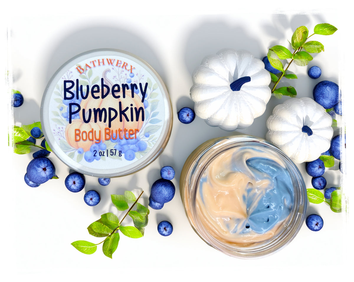 BathWerx Blueberry Pumpkin Body Butter, 2 oz jar shown open with a peach and blue swirled body butter, displayed with white decorative pumpkins, fresh blueberries, and green leaves on a white surface.