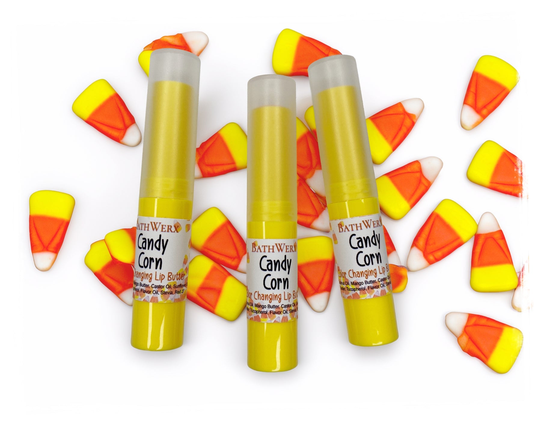 Three BathWerx Candy Corn Color-Changing Lip Butter tubes in yellow packaging surrounded by candy corn pieces on a white background.