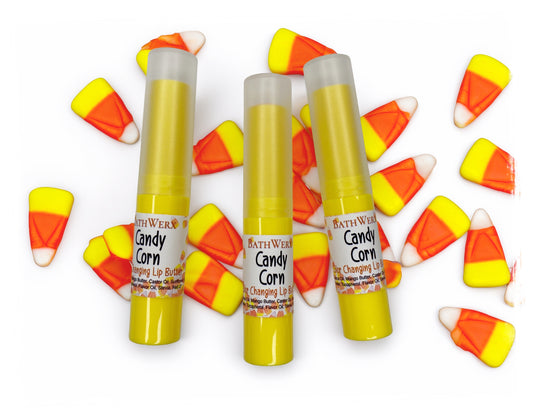 Three BathWerx Candy Corn Color-Changing Lip Butter tubes in yellow packaging surrounded by candy corn pieces on a white background.