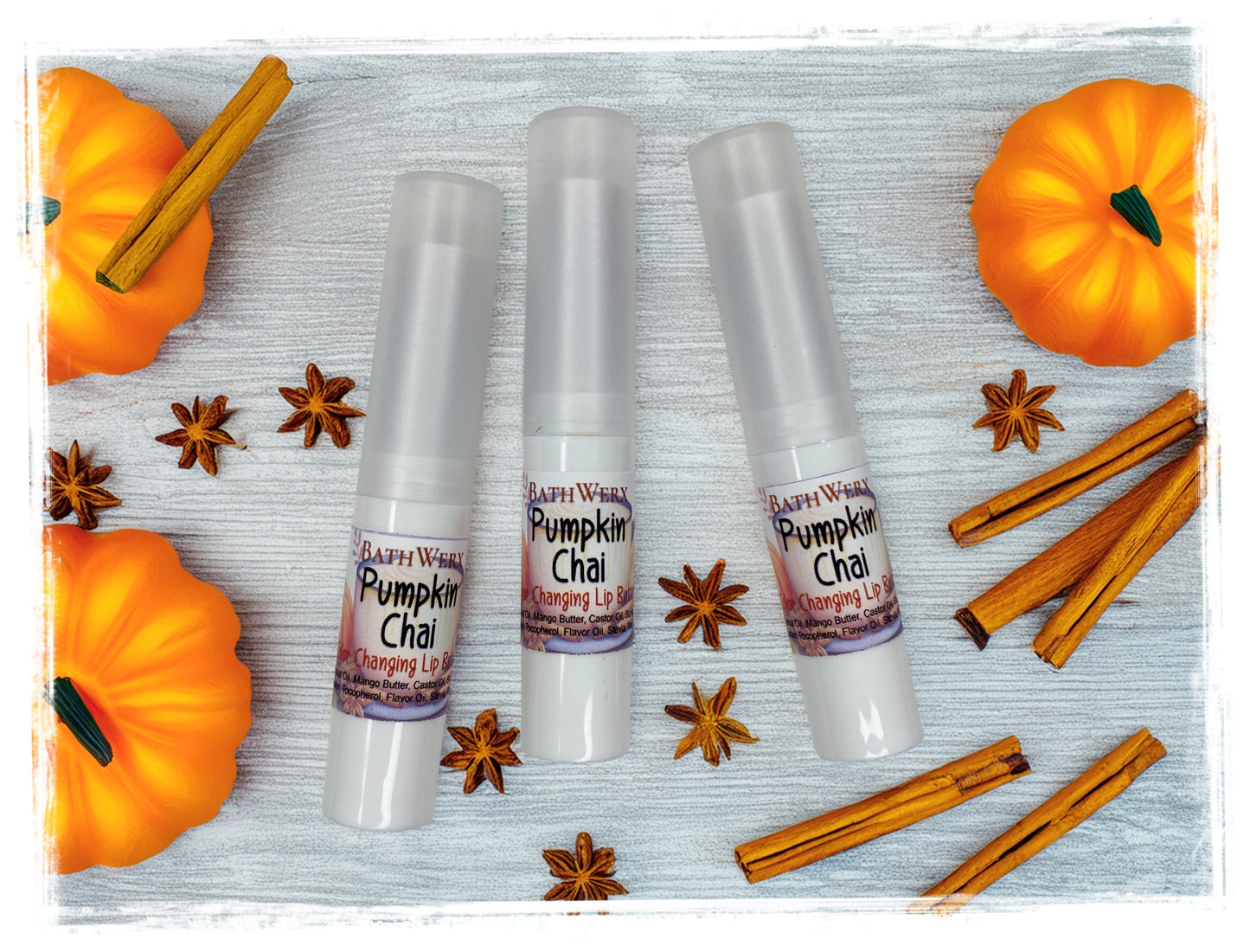 Three BathWerx Pumpkin Chai Color-Changing Lip Butter tubes in white packaging with star anise, cinnamon sticks, and orange pumpkins on a white wood background.