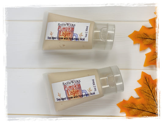 Two mini 1oz tubes of BathWerx Pumpkin Lager Shea Hand Cream with Hyaluronic Acid on a white wood background with fall maple leaves.
