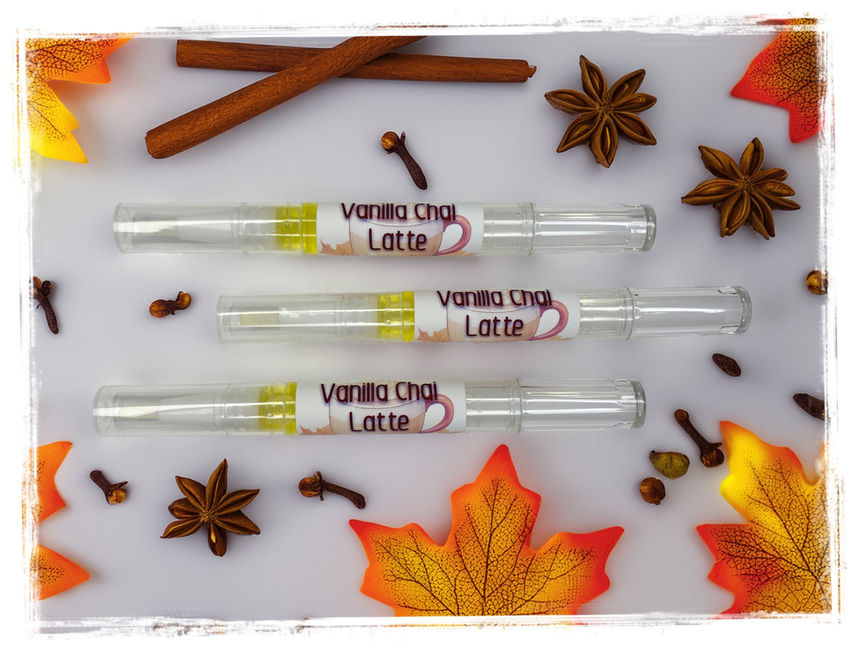 Three Vanilla Chai Latte nail cuticle pens arranged on a white surface with fall maple leaves, star anise, cinnamon sticks, and cloves.