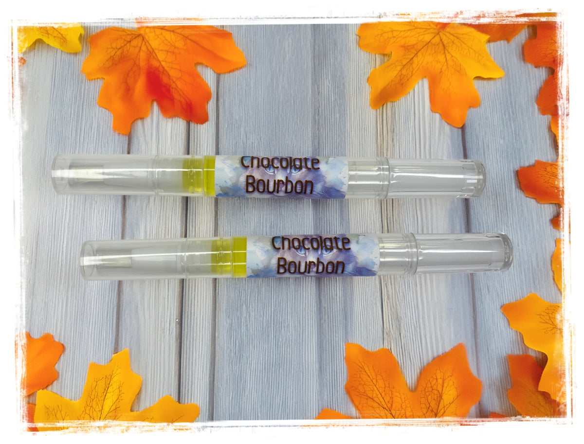 Two Chocolate Bourbon nail cuticle pens on a light blue wood surface surrounded by fall maple leaves.
