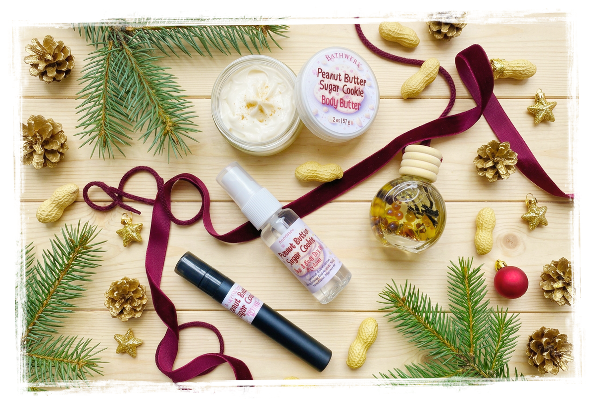 Peanut Butter Cookie body butter, dry oil, perfume spray, and car charm on pale wood with scattered peanuts, burgundy ribbon, evergreen branches, and gold holiday accents.
