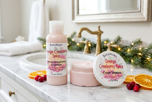 Orange Cranberry Spice shampoo and conditioner on a marble bathroom vanity with evergreen garland, holiday lights, orange slices, and cranberries.